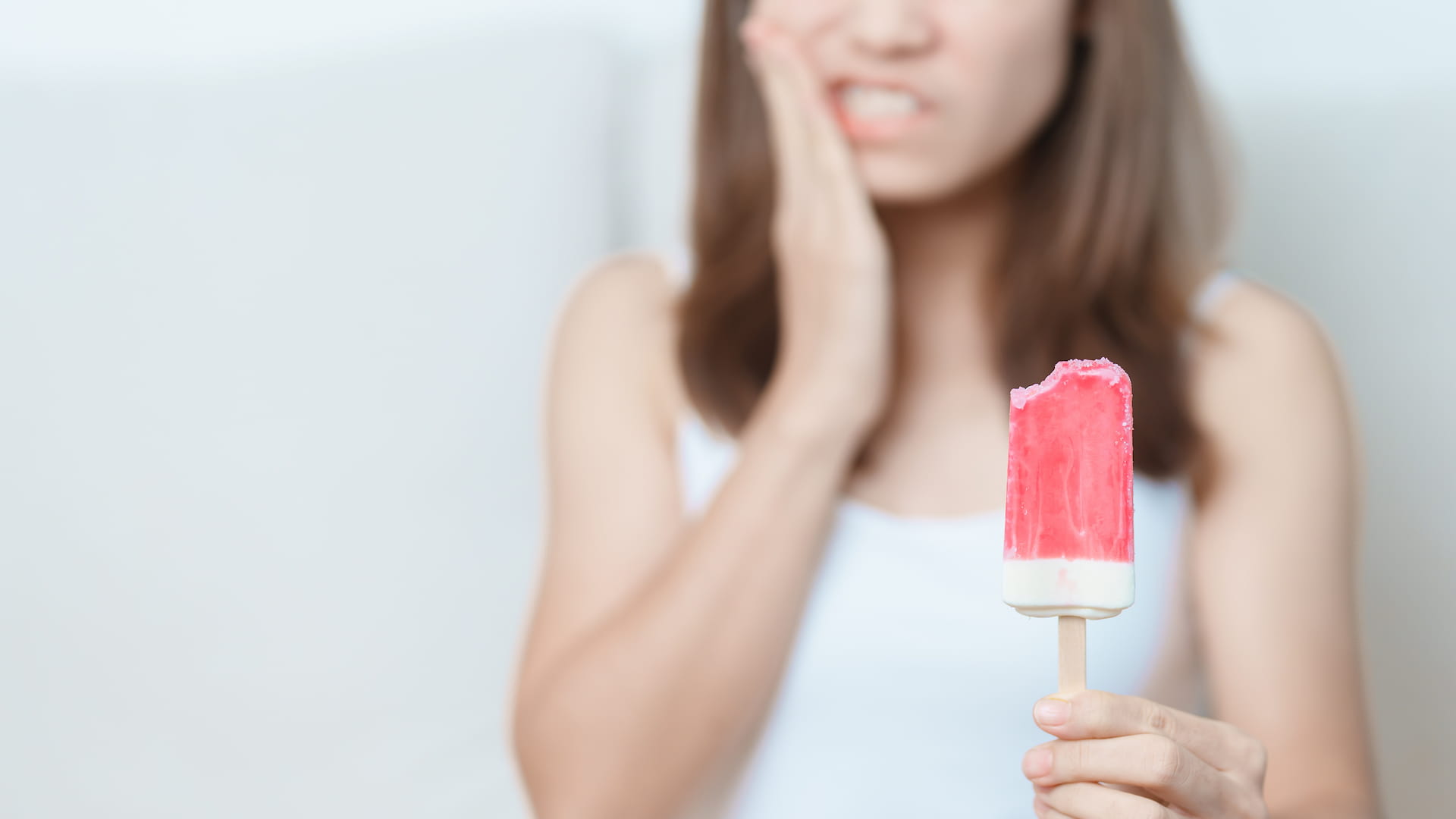 Girl eating ice cream with pain in mouth experiencing symptoms of tooth erosion